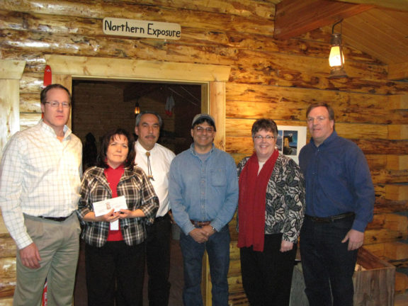 Group standing inside of museum cabin holding check