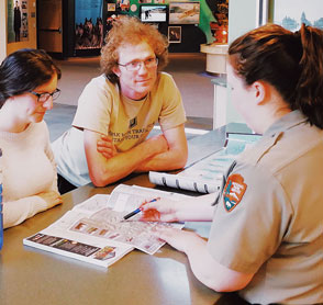 man and woman speak with national park ranger at information desk